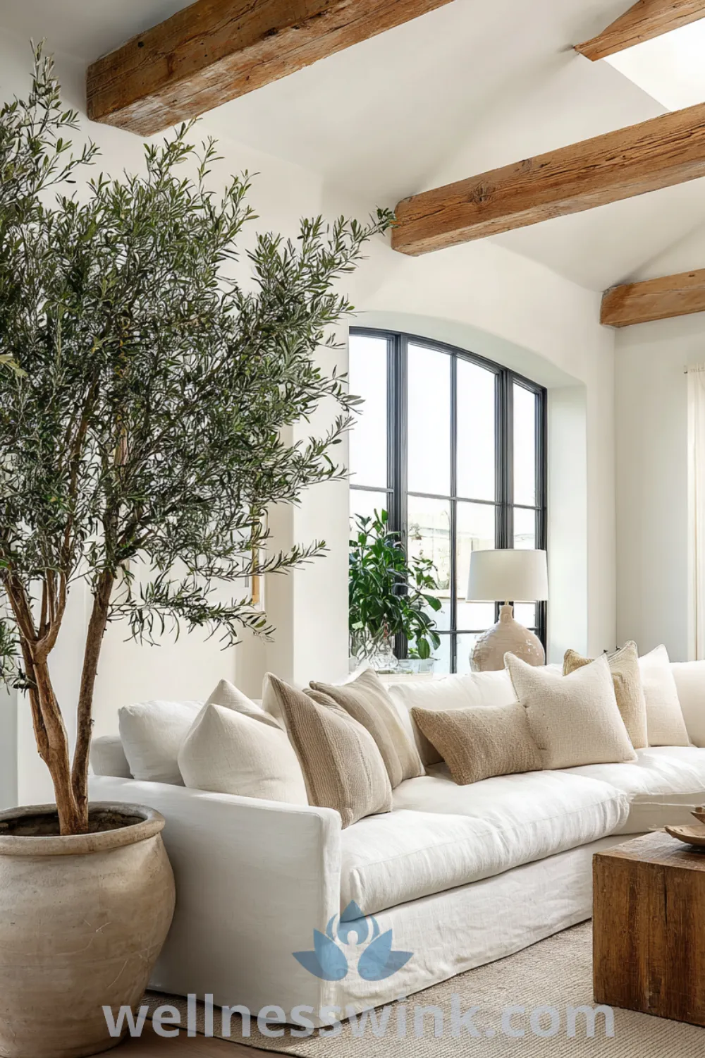Bright modern farmhouse living room with oversized sectional sofa, large olive tree, exposed wooden beams, and cozy jute rug decor ideas.